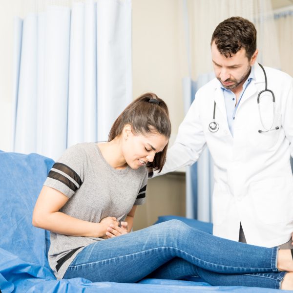 Beautiful young woman having severe stomach ache visiting doctor for treatment
